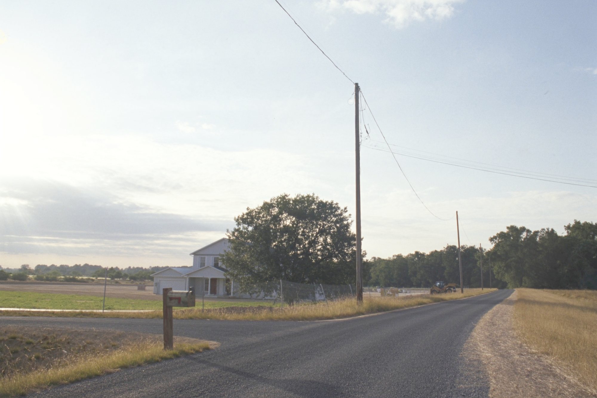 A gravel county road at sunrise, a new house set back on acreage where construction meets farm ground.