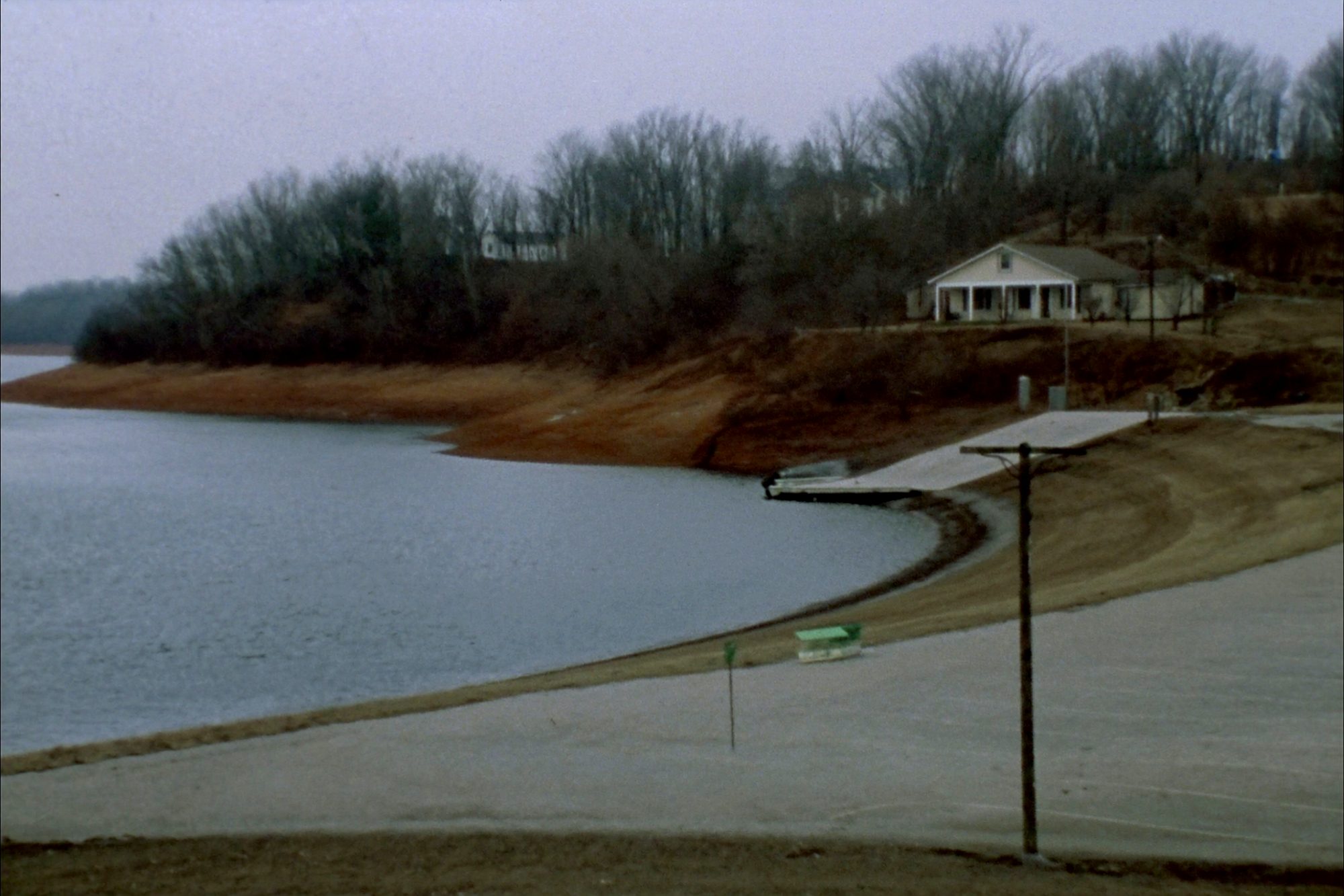 A grey afternoon on a Missouri reservoir, houses set back among bare oaks on the bluff above the water.