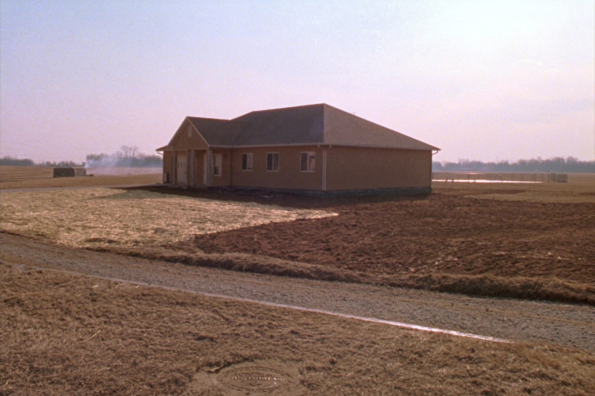 A newly finished house alone on a bare graded acreage lot, gravel drive and open farm ground beyond.